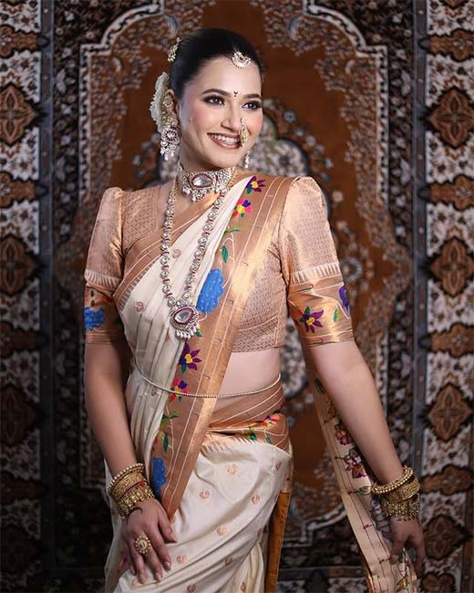 Woman in cream Nauvari saree with floral embroidery and statement jewellery.