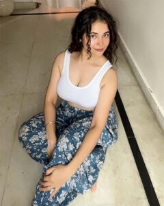 Beautiful Indian desi bhabhi photo in stylish white top and printed pajama sitting pose.