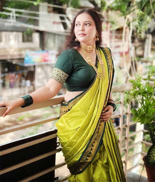 Woman in parrot green Nauvari saree with dark green blouse and gold jewellery.