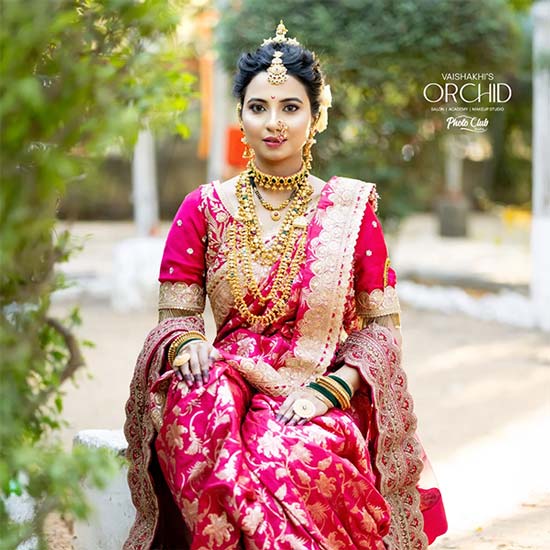 Woman in pink Nauvari saree with golden embroidery and layered traditional jewellery.