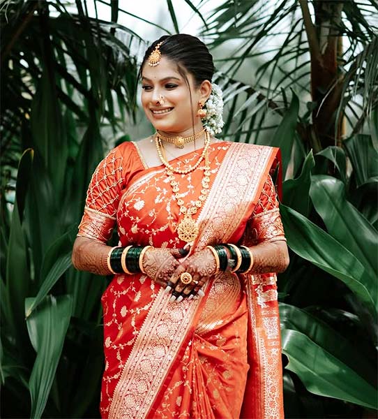 Marathi bride in red Nauvari saree with golden border and traditional jewellery.