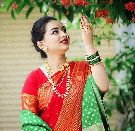 Woman in red and green Nauvari saree with gold jewellery and green bangles.