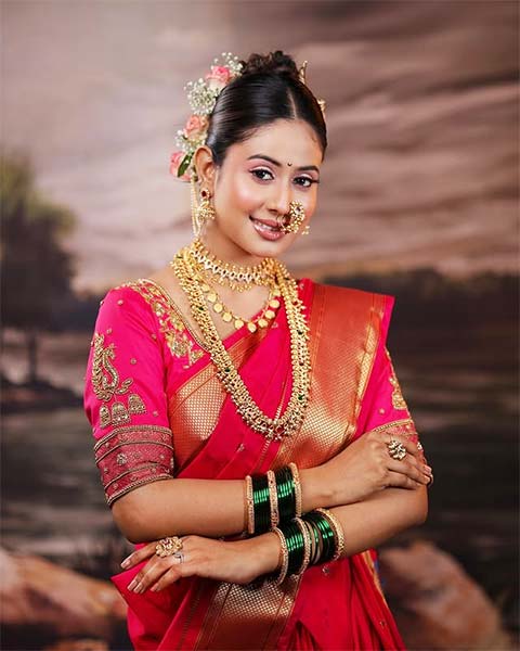 Woman in pink Nauvari saree wearing gold jewellery and green bangles.